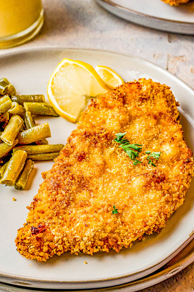 Breaded chicken cutlet with lemon slices and green beans on a plate.