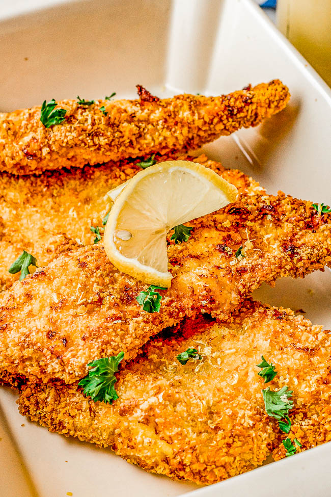 Crispy breaded chicken cutlets garnished with parsley and a lemon slice, served in a white dish.