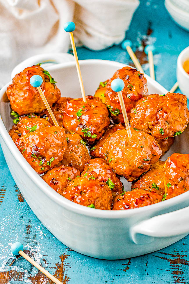 A white dish filled with glazed meatballs, each with a blue-tipped toothpick inserted, placed on a blue wooden surface.