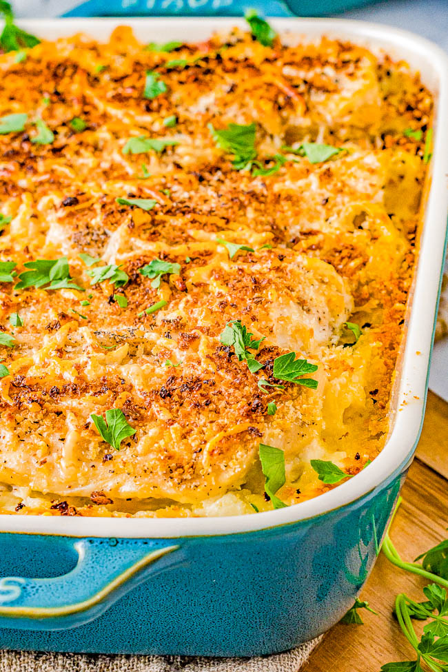 A casserole dish filled with baked golden-brown scalloped potatoes, garnished with parsley, in a blue rectangular baking dish.