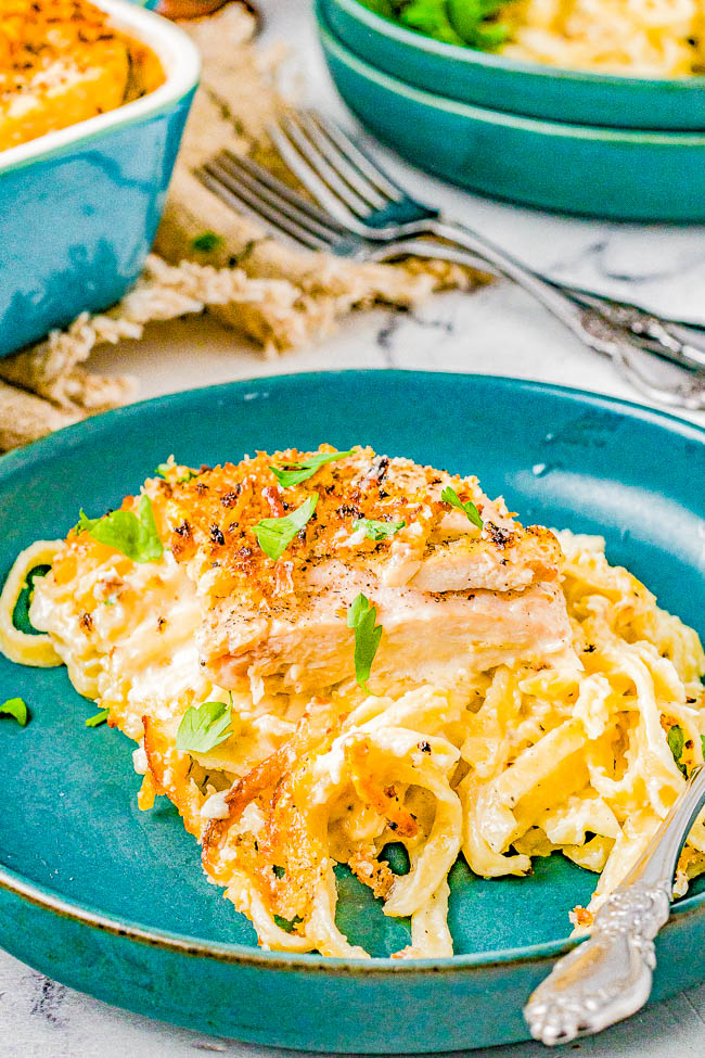 A serving of creamy chicken Alfredo pasta garnished with herbs on a blue plate, accompanied by a fork and a napkin in the background.