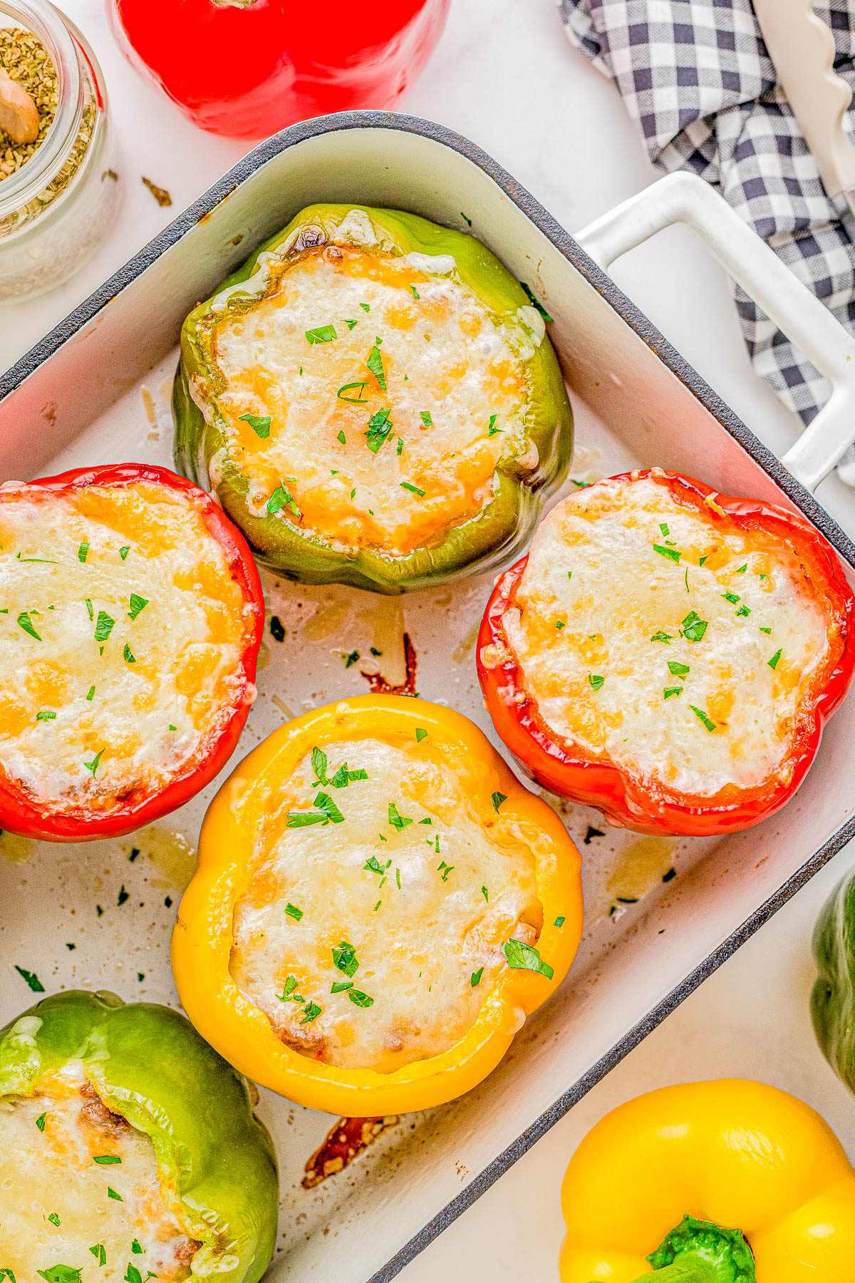 Baked bell peppers stuffed with cheese and garnished with herbs in a rectangular baking dish.