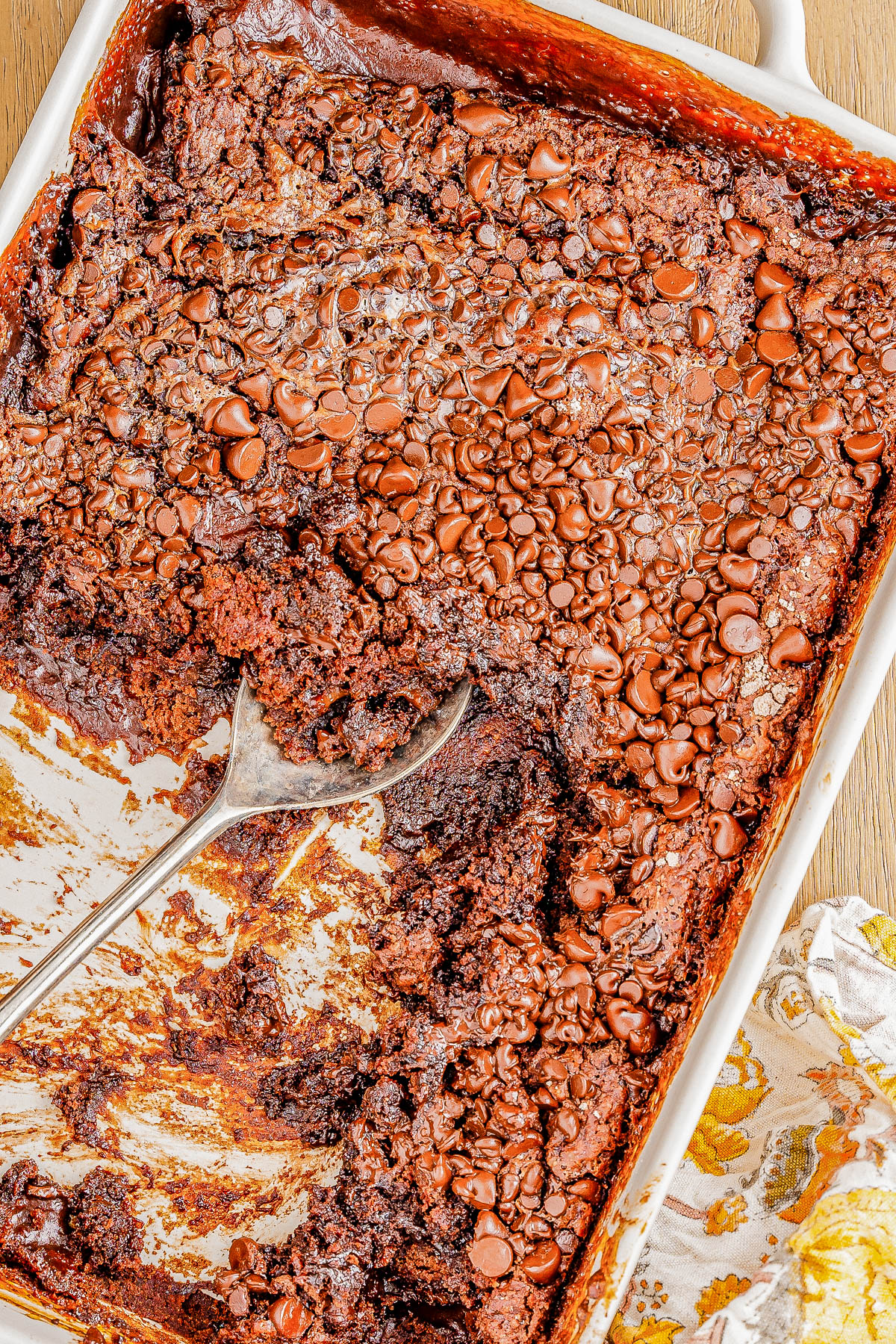 A partially eaten chocolate dessert with a spoon in a baking dish, topped with melted chocolate chips.