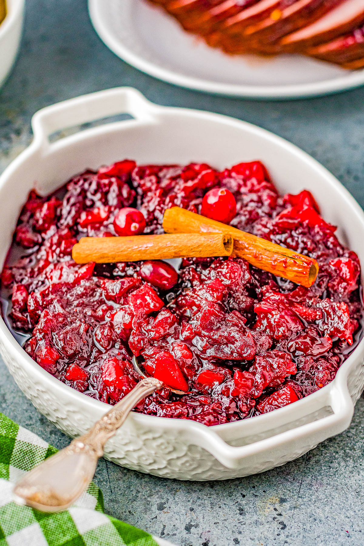 A white ceramic dish filled with cranberry sauce, garnished with two cinnamon sticks, placed on a table.