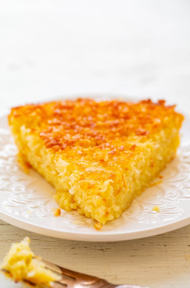 A slice of golden coconut pie on a white plate, with a bite taken out shown on a fork in the foreground.