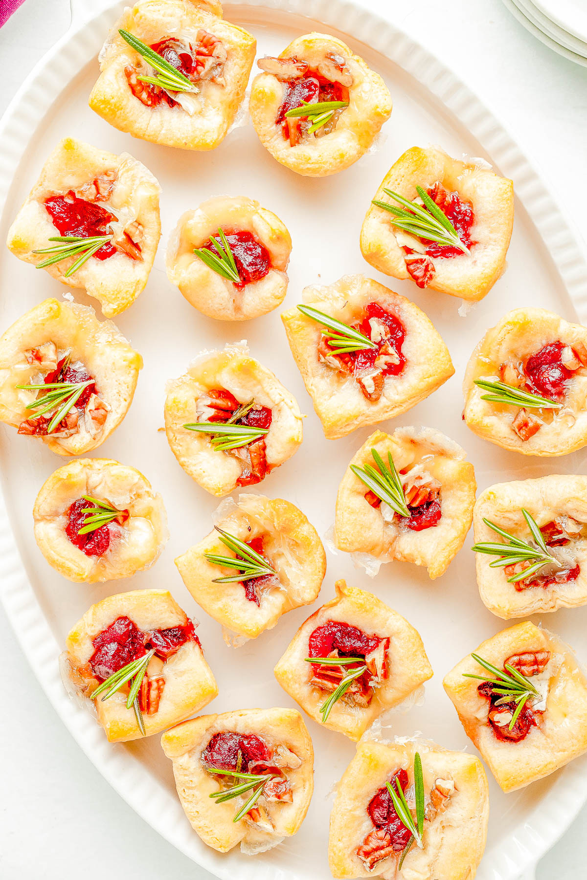 A white plate with several bite-sized pastry appetizers topped with red sauce, cheese, and small green herb sprigs.