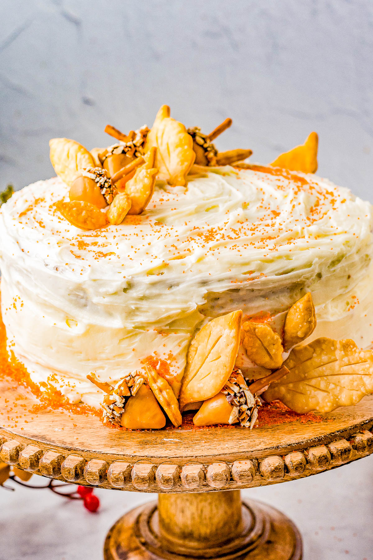 A frosted cake topped with decorative cookie leaves and sprinkled with orange-colored sugar, displayed on a wooden cake stand.