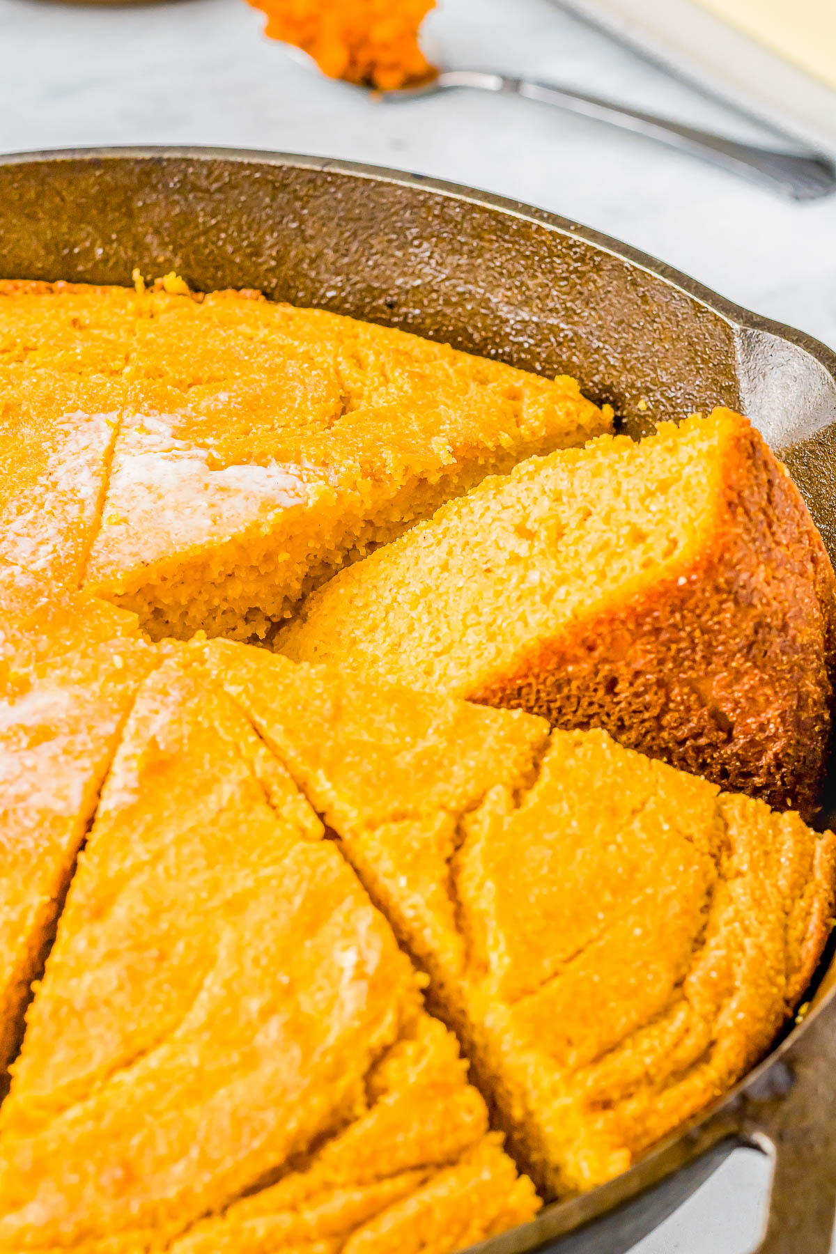 A sliced cornbread in a cast iron skillet, showing a golden brown crust and a moist interior.