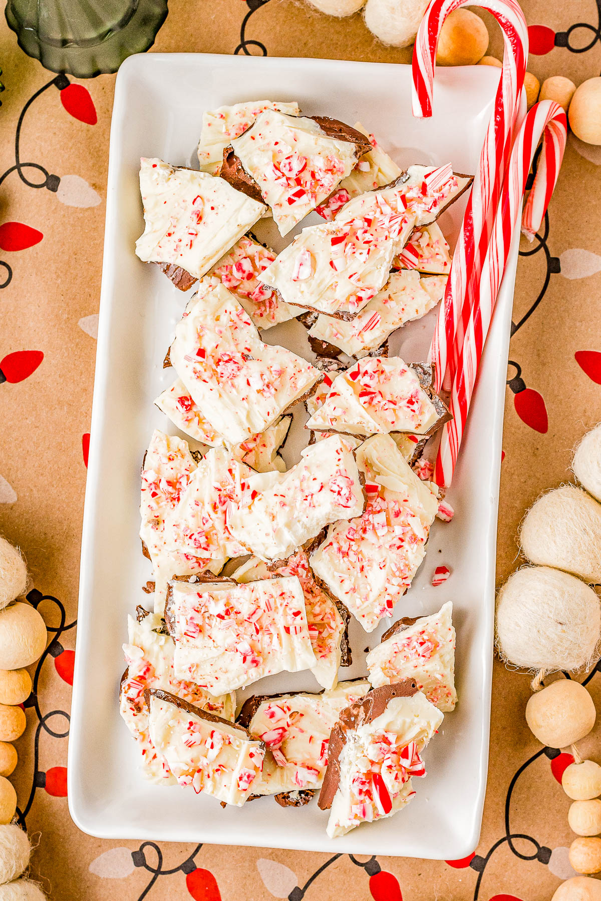 A rectangular platter with pieces of peppermint bark topped with crushed candy canes, accompanied by two whole candy canes.