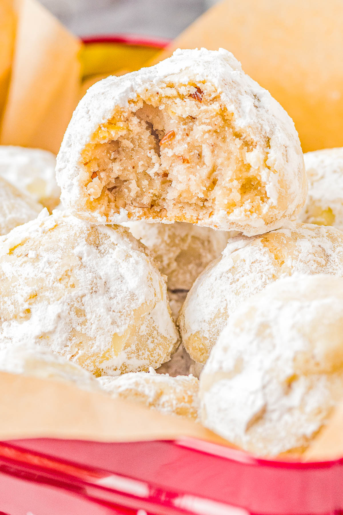 A basket of powdered sugar-coated cookies, one with a bite taken out, revealing a nutty, crumbly interior.