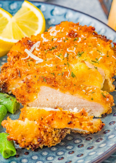 Breaded chicken cutlet topped with lemon glaze and garnished with herbs on a plate.