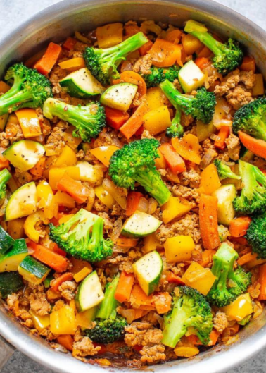A colorful stir-fry with broccoli, carrots, zucchini, and ground meat in a pan.