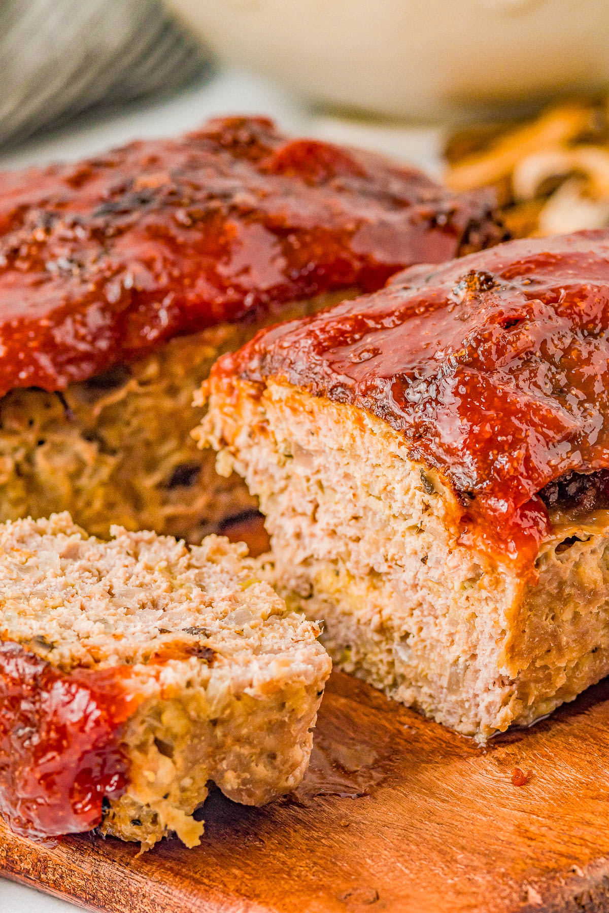 Close-up of a sliced meatloaf with a glossy red sauce glaze, placed on a wooden board.