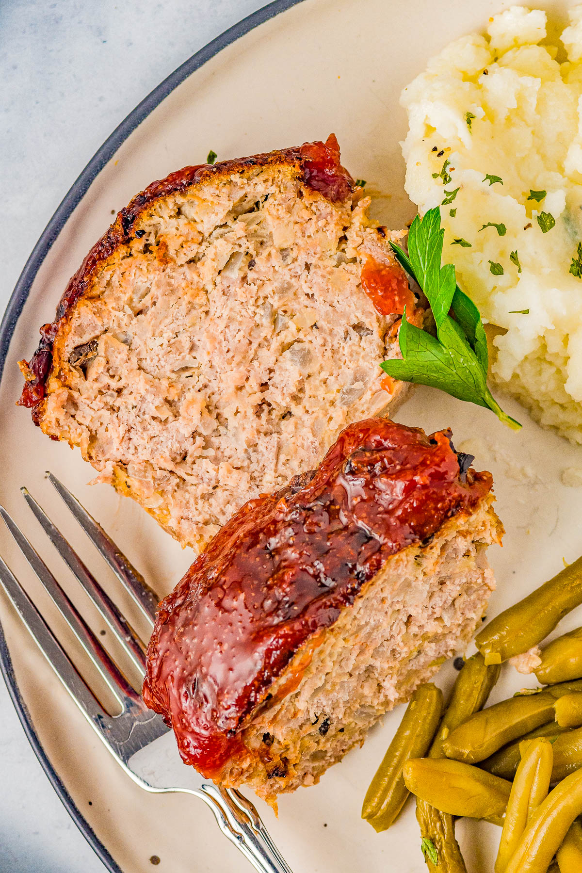 Plate with two slices of glazed meatloaf, a scoop of mashed potatoes, green beans, and a fork.