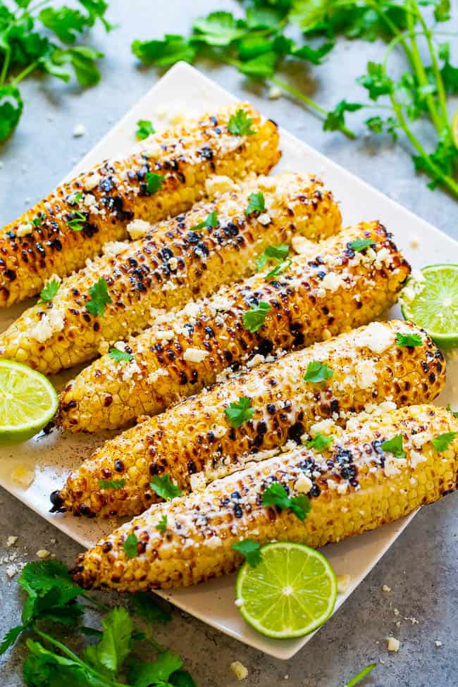 Grilled corn on the cob garnished with herbs and spices on a serving plate.