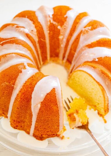 A sliced lemon bundt cake with white glaze on a glass plate with a fork.