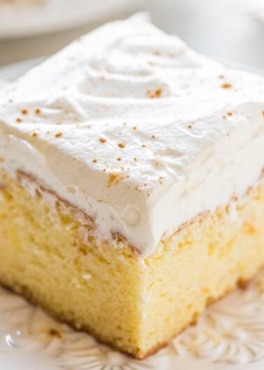 A slice of frosted vanilla cake on a white plate.