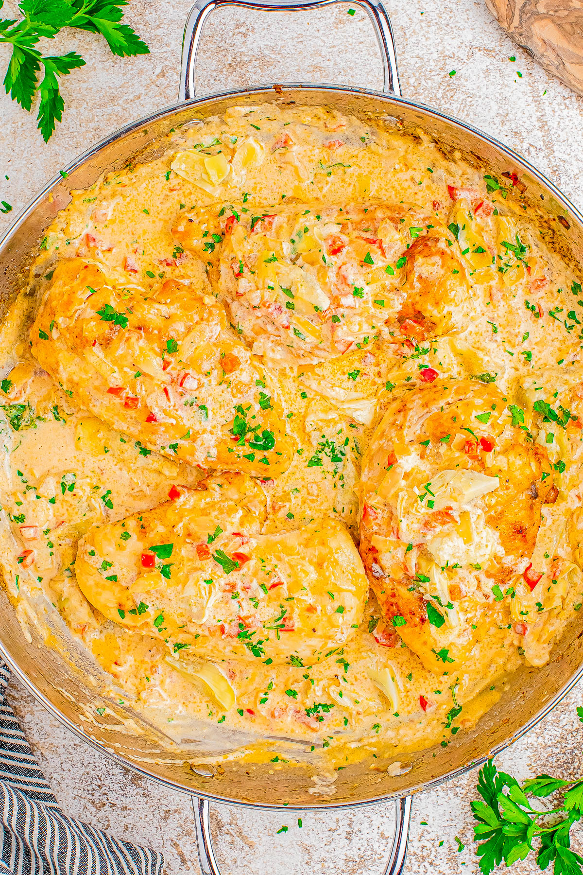 Chicken breasts in a creamy sauce with herbs, onions, and peppers in a large skillet.