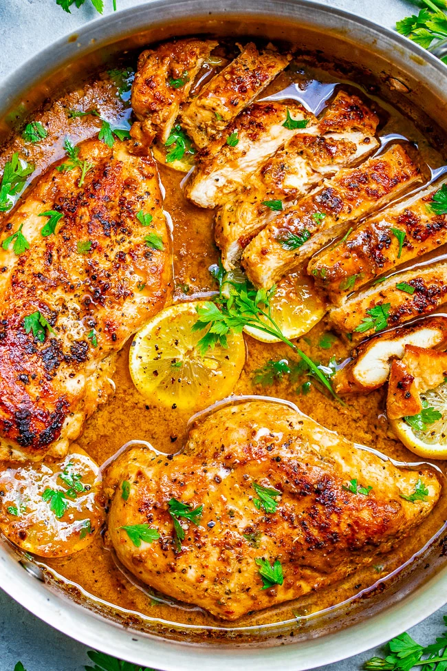 Pan-seared chicken breasts in a lemon herb sauce, garnished with parsley, in a skillet.