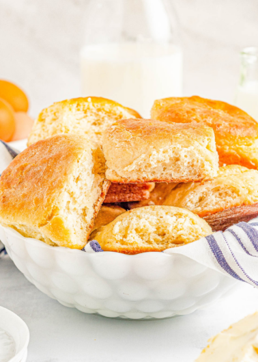 A bowl of freshly baked biscuits with a side of milk and eggs.