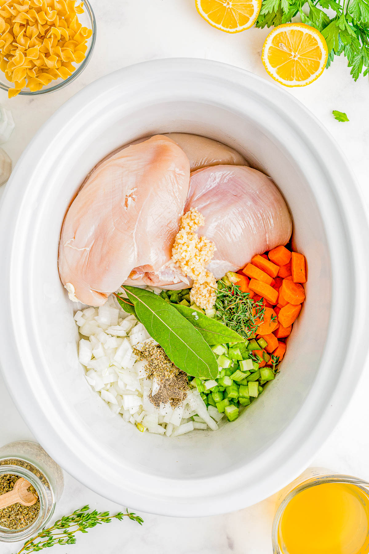 Raw chicken, veggies, and herbs in a slow cooker. 