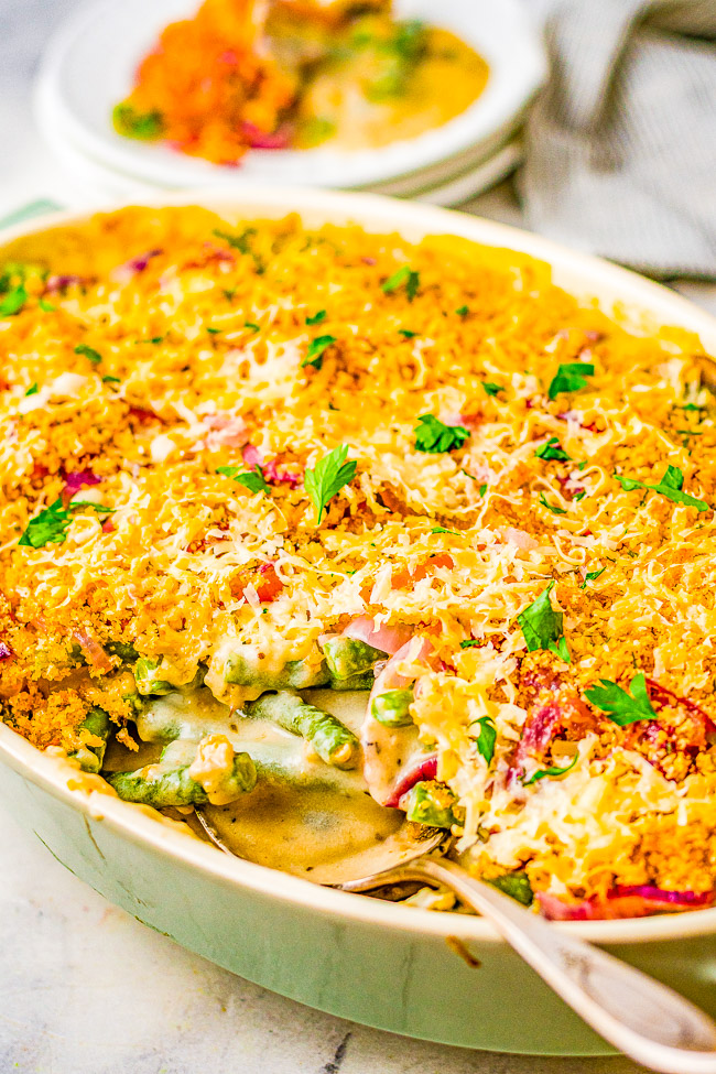 A close-up of a baked casserole dish with a golden breadcrumb topping, garnished with herbs. A portion of the dish is served on a plate in the background.