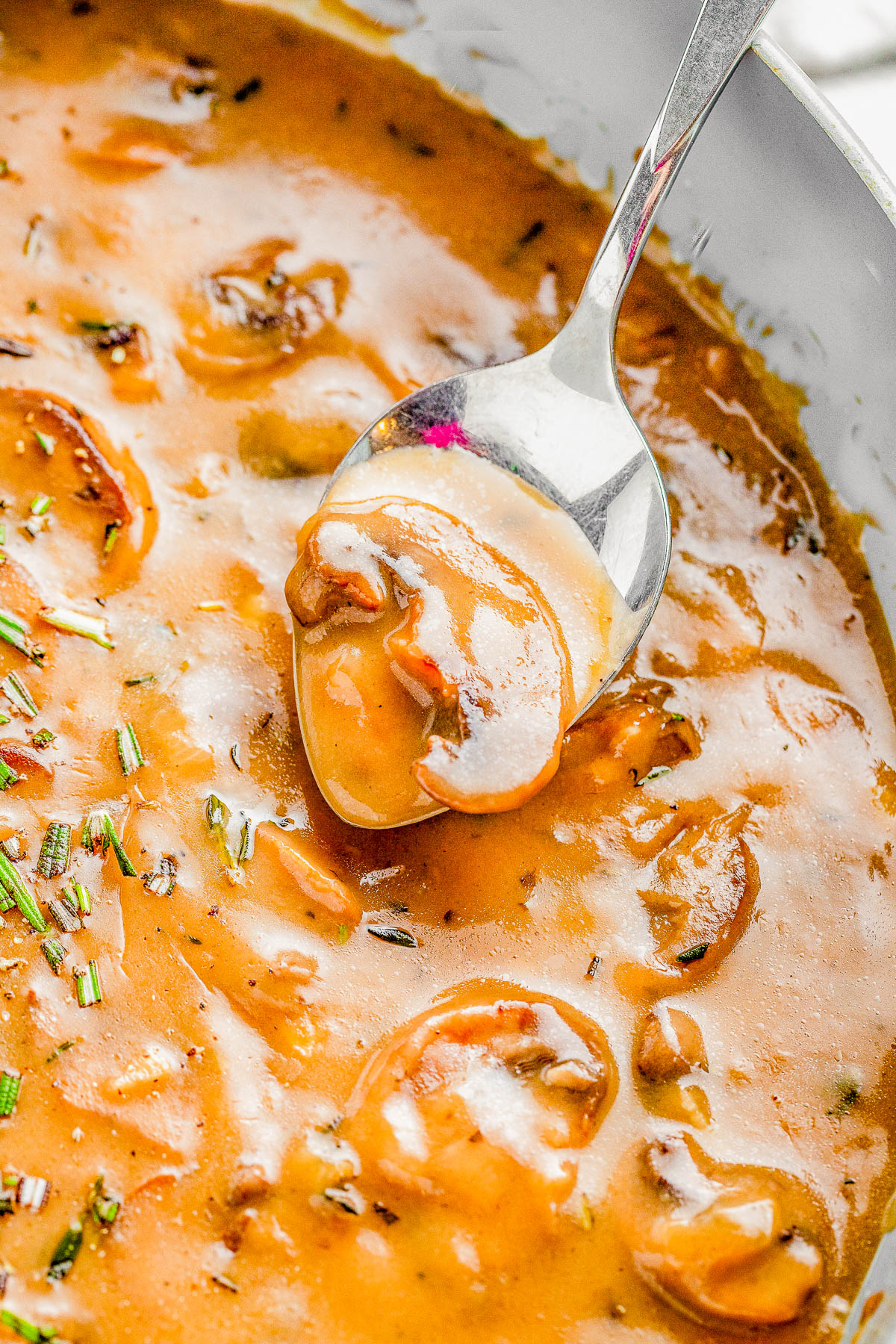 Close-up of a spoonful of creamy mushroom soup in a bowl. The soup has visible mushroom slices and is garnished with chopped herbs.