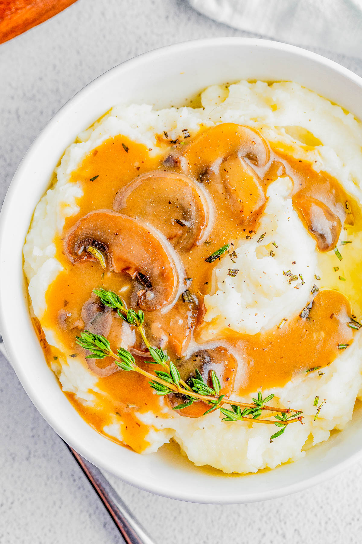 A bowl of mashed potatoes topped with brown mushroom gravy and garnished with fresh herbs.