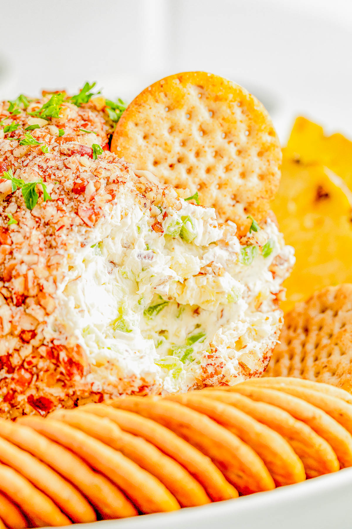 Cheese ball coated with chopped nuts, surrounded by assorted crackers, with a cracker placed on top.