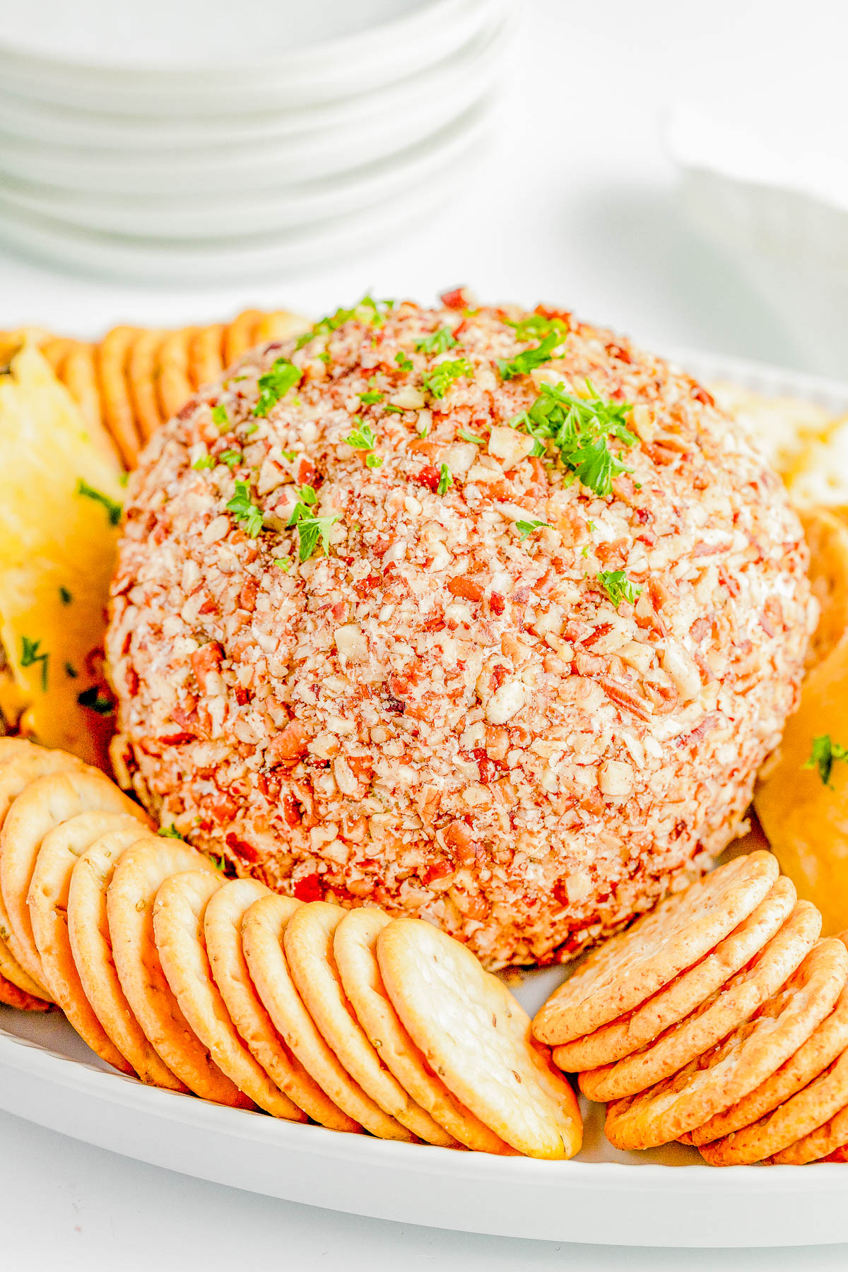 Cheese ball coated with chopped nuts, garnished with herbs, surrounded by crackers on a plate.