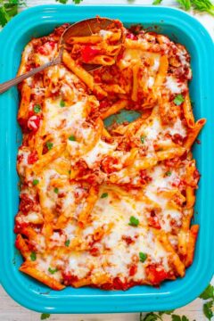 Baked ziti with melted cheese and tomato sauce in a blue dish, garnished with herbs.