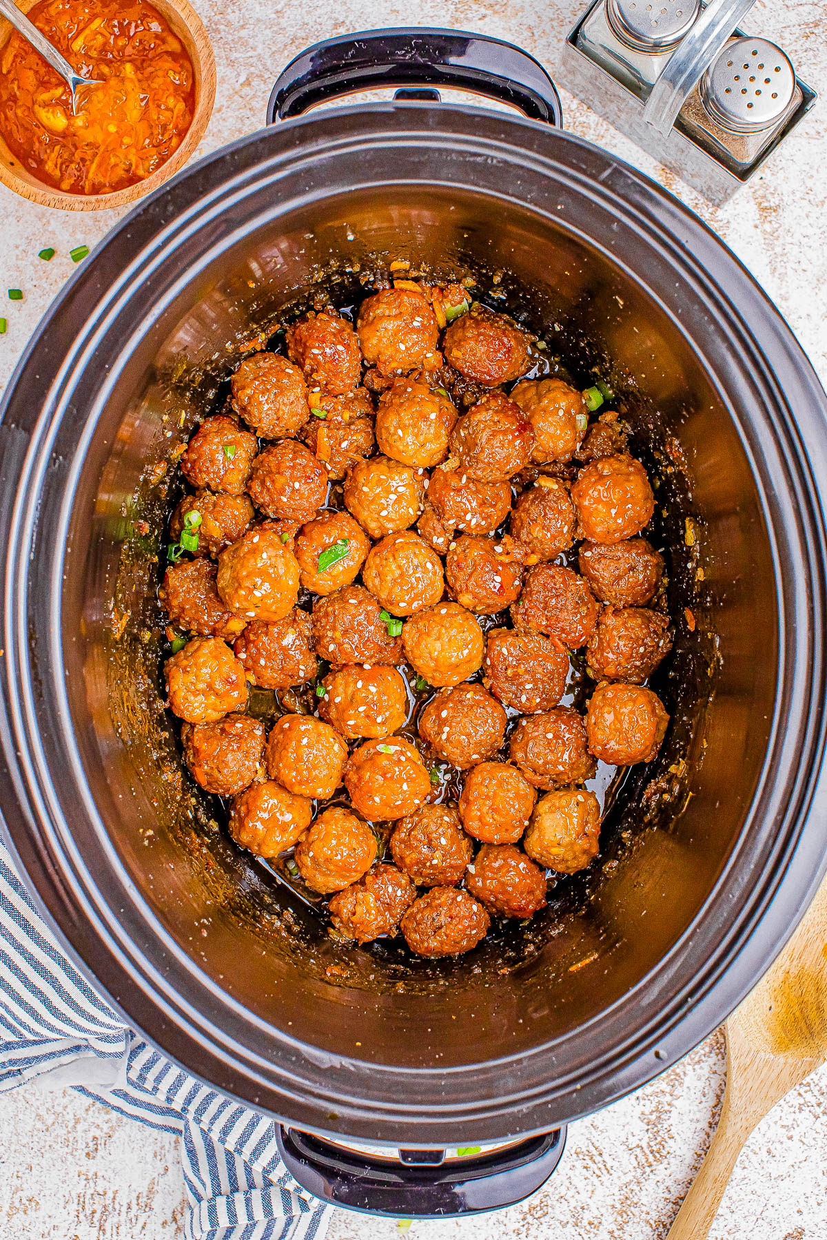Top view of a slow cooker filled with glazed meatballs sprinkled with green onions.