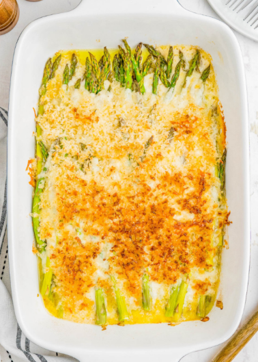 A baking dish filled with baked asparagus topped with melted cheese and breadcrumbs.