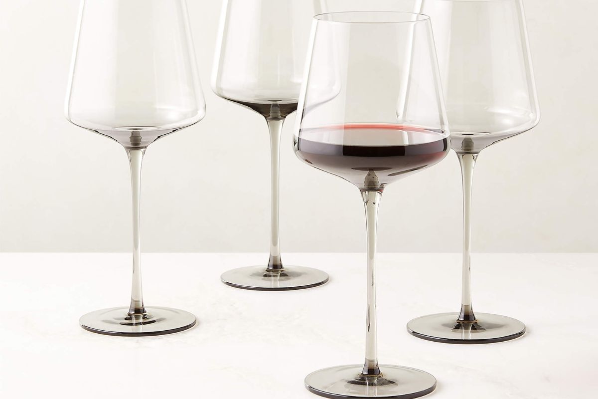 Four empty wine glasses and one partially filled with red wine are arranged on a white surface.