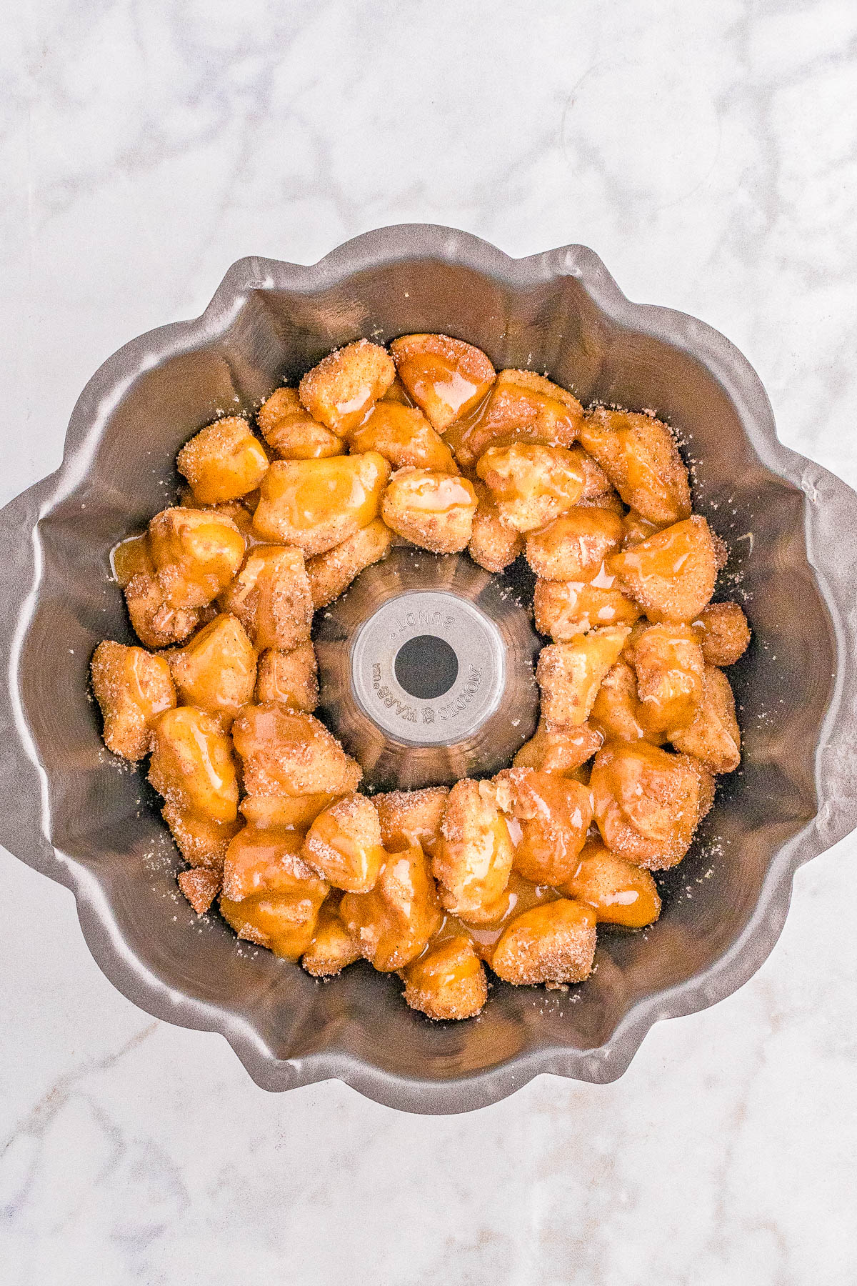 Caramel-glazed monkey bread pieces arranged in a circular fluted tube pan on a marble surface.