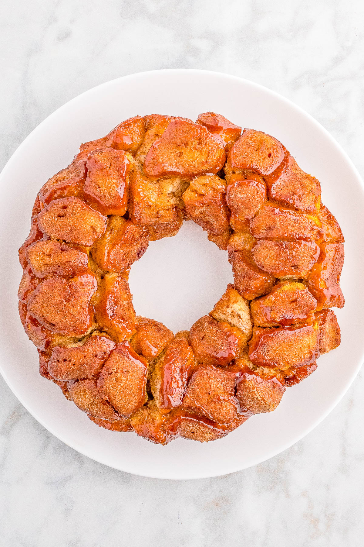 A large monkey bread on a white plate, featuring golden-brown, sugar-coated dough pieces arranged in a circular wreath shape.