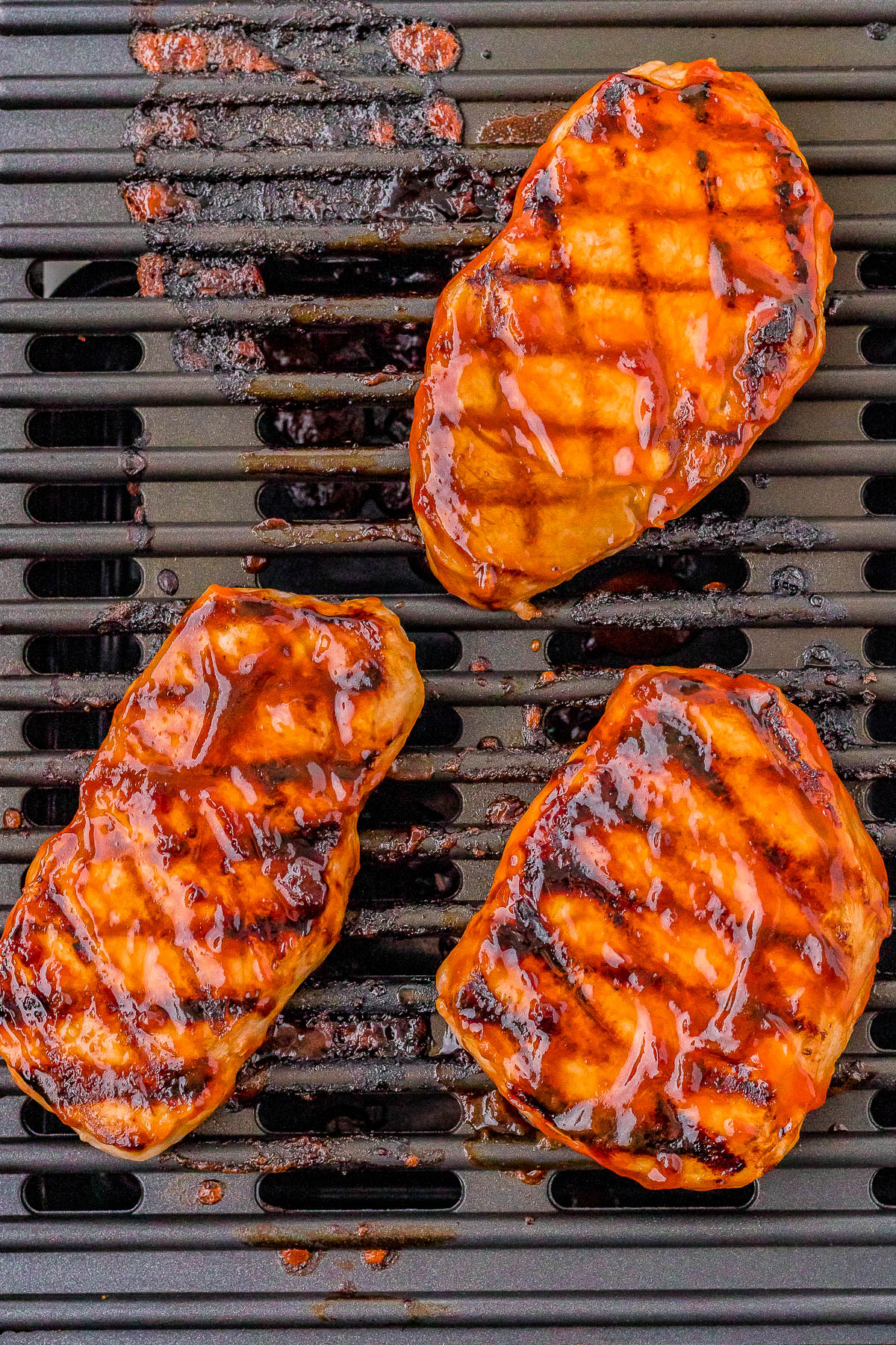 Three pieces of grilled, glazed barbecue pork on a grill grate, showing char marks and a shiny coating of sauce.