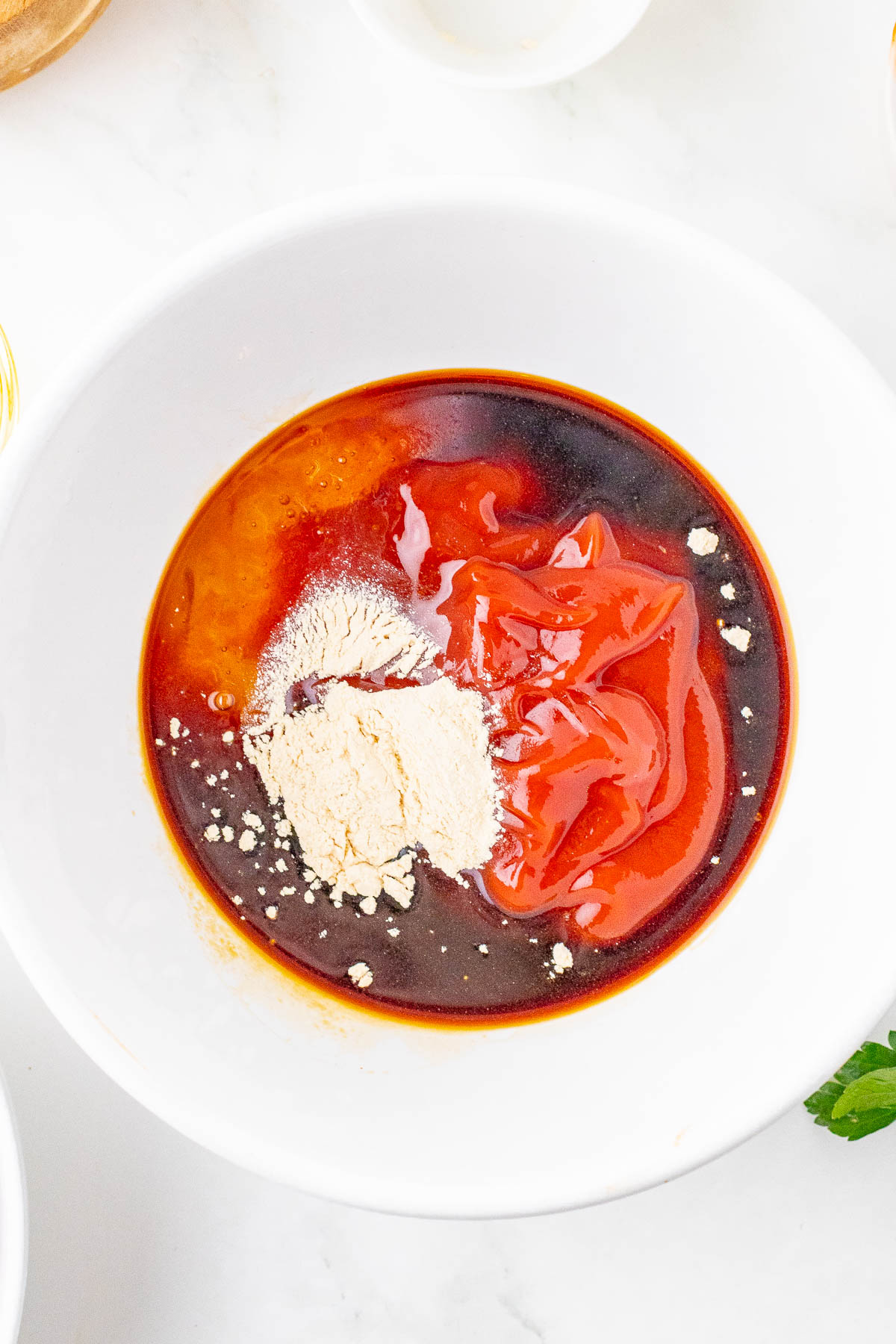 A white bowl contains red sauce, a brown liquid, and a white powder on a white background.