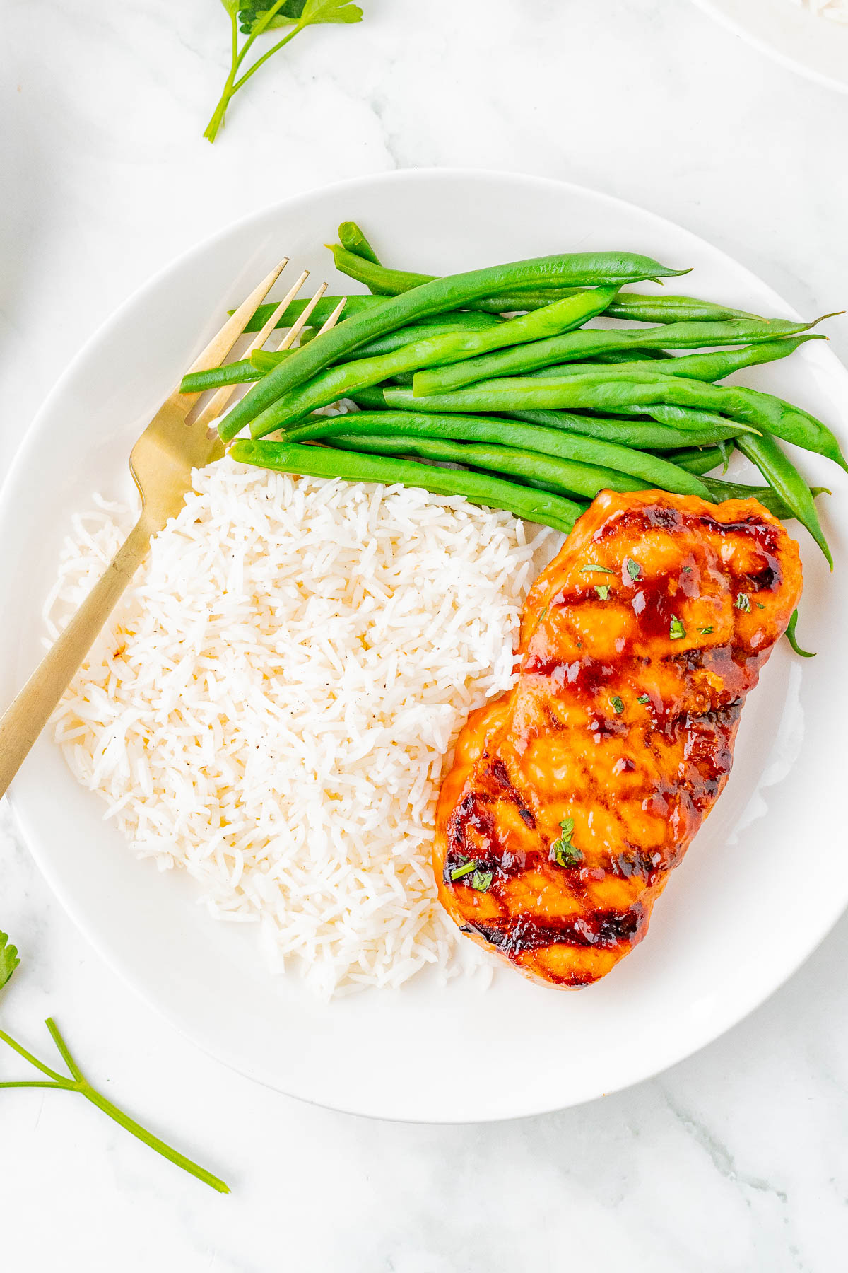 A plate of white rice, grilled glazed pork, and green beans with a gold-colored fork on the side.