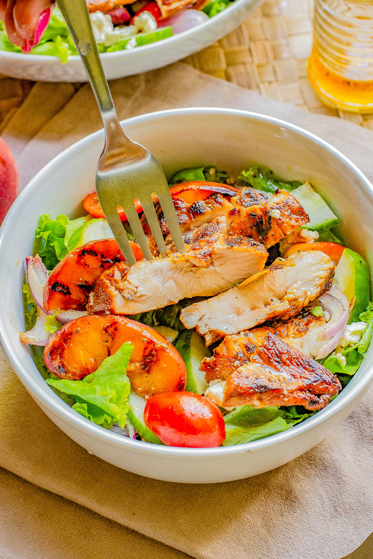 A bowl of salad with grilled chicken slices, cherry tomatoes, avocado pieces, and red onion, with a fork placed in the middle.
