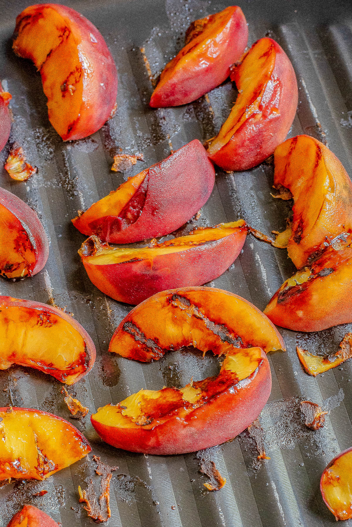 Close-up of grilled peach slices on a grill pan, with caramelized edges and grill marks visible on the fruit's surface.