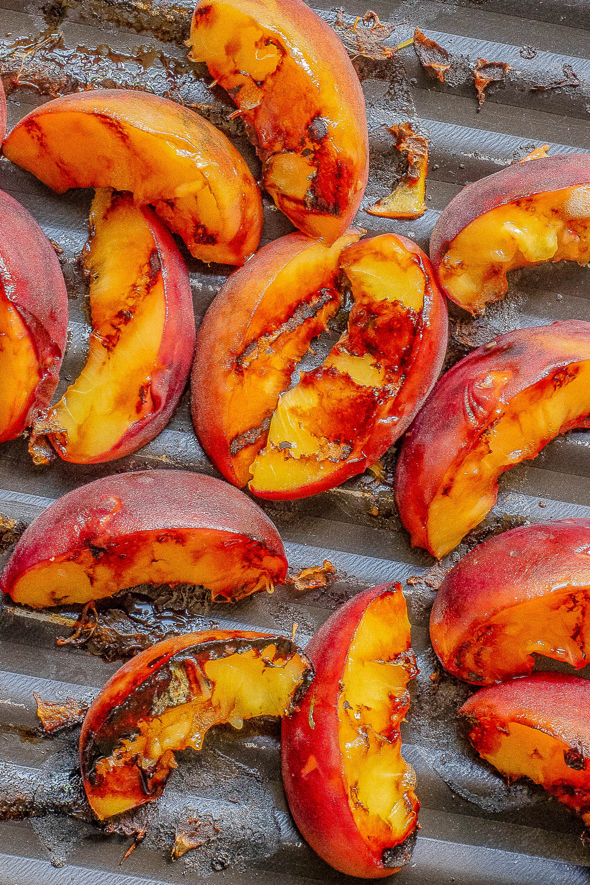 Close-up of grilled peach halves with char marks on a metal grill plate.