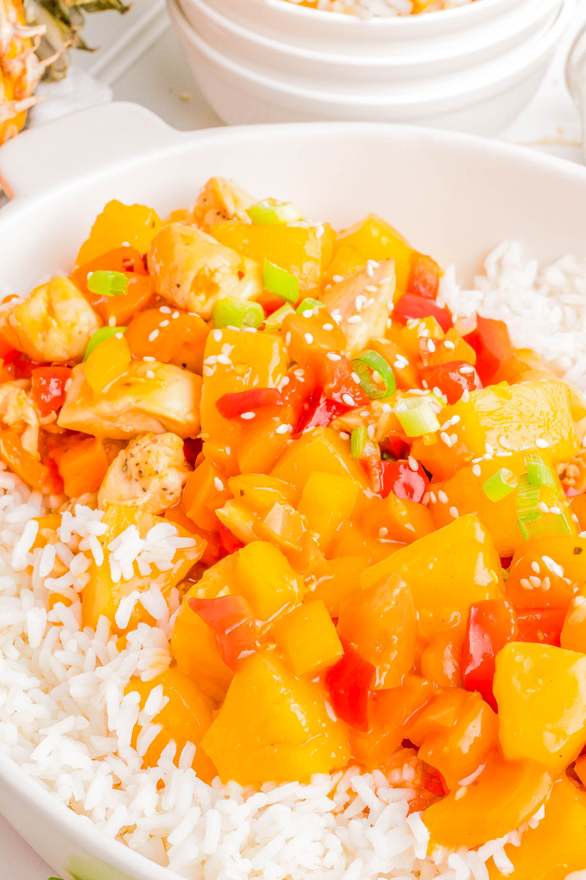 A plate of white rice topped with diced chicken, bell peppers, pineapple chunks, and green onions in a savory-sweet sauce, garnished with sesame seeds.