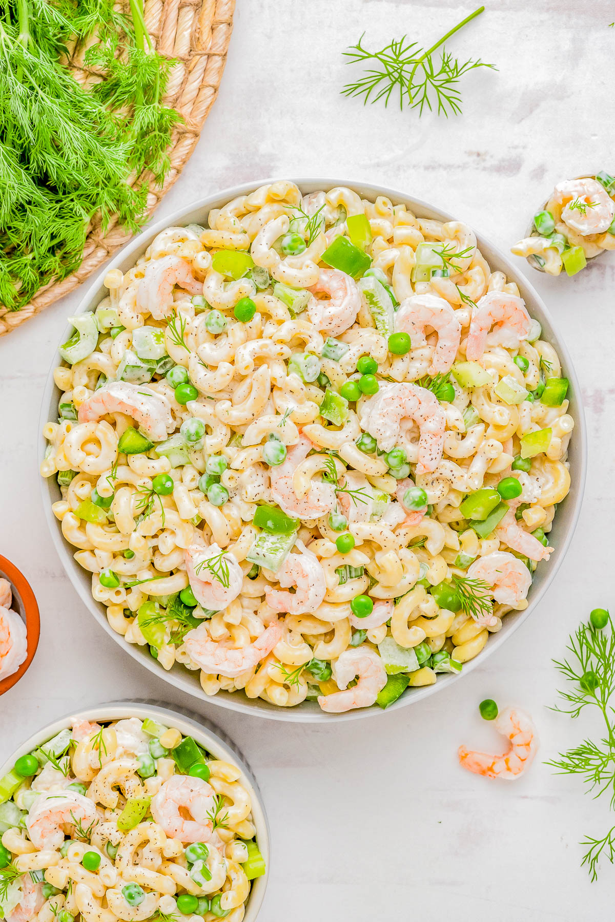 A colorful shrimp pasta salad with green peas, chopped celery, and dill, served in a large white bowl, garnished with fresh herbs.