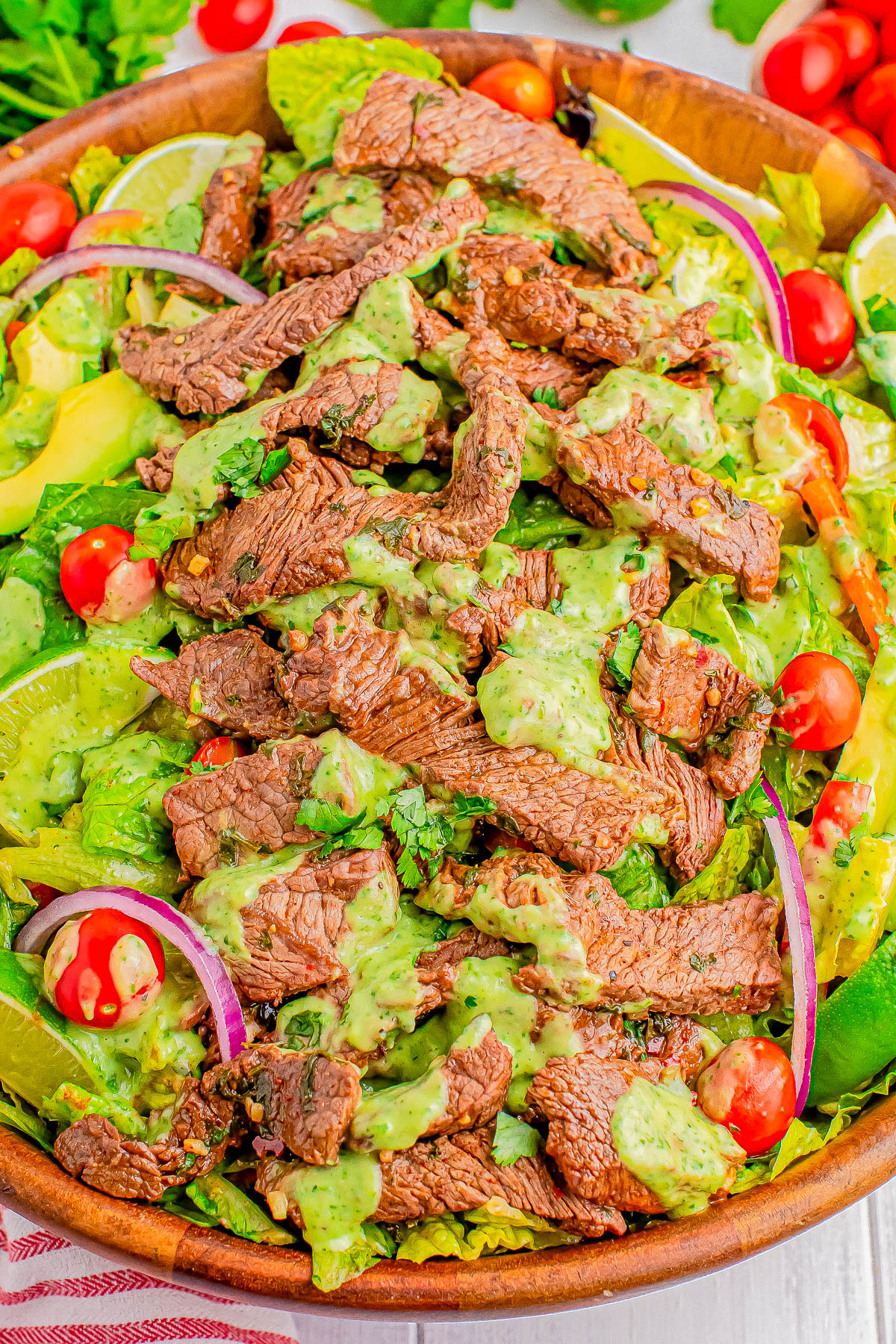 A salad featuring sliced grilled steak, cherry tomatoes, red onion, avocado, and greens drizzled with a creamy green dressing.