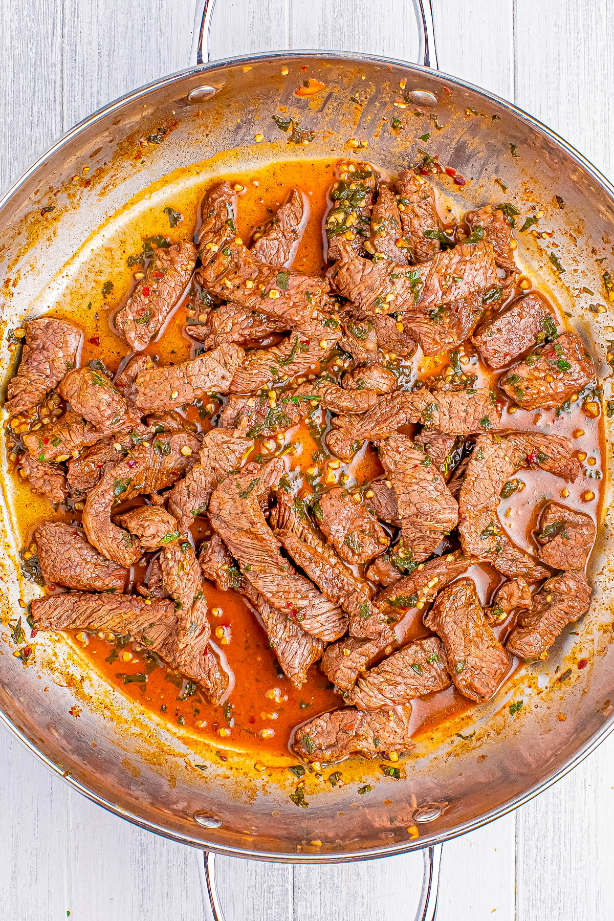 A pan filled with cooked strips of beef in a red sauce, garnished with herbs and spices.