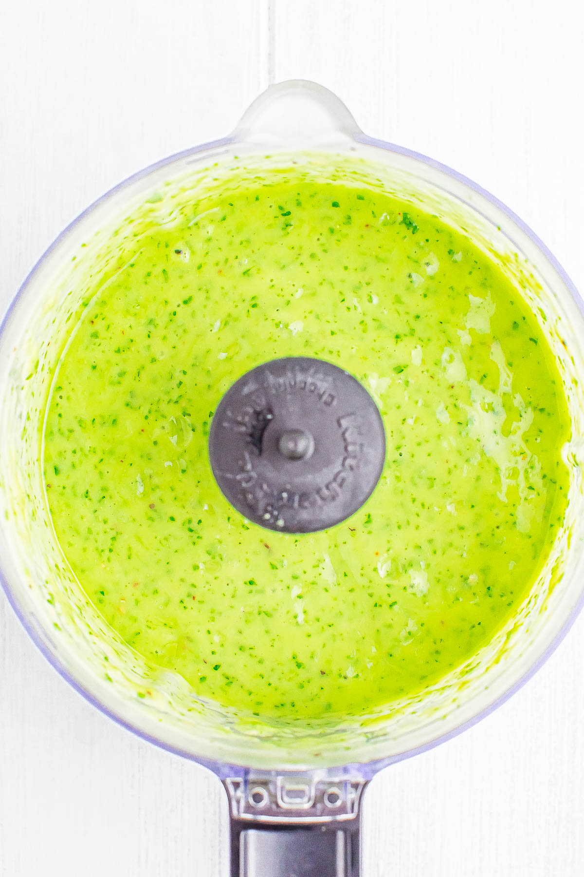 A top view of a food processor bowl containing a blended green sauce.