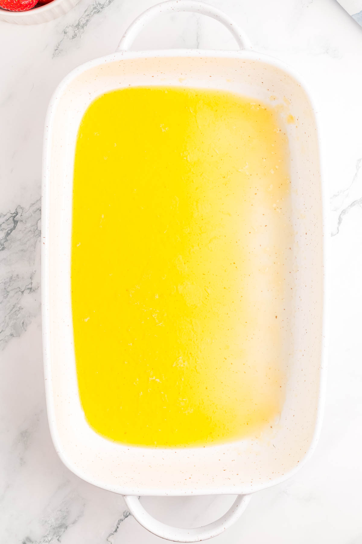 Rectangular white baking dish filled with melted butter on a marble countertop.