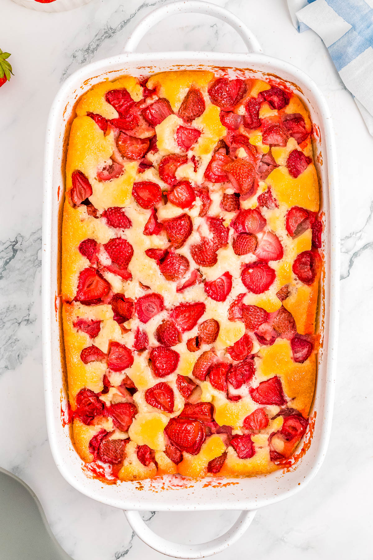 Baked dessert in a white dish with sliced peaches and strawberries on a marble surface.
