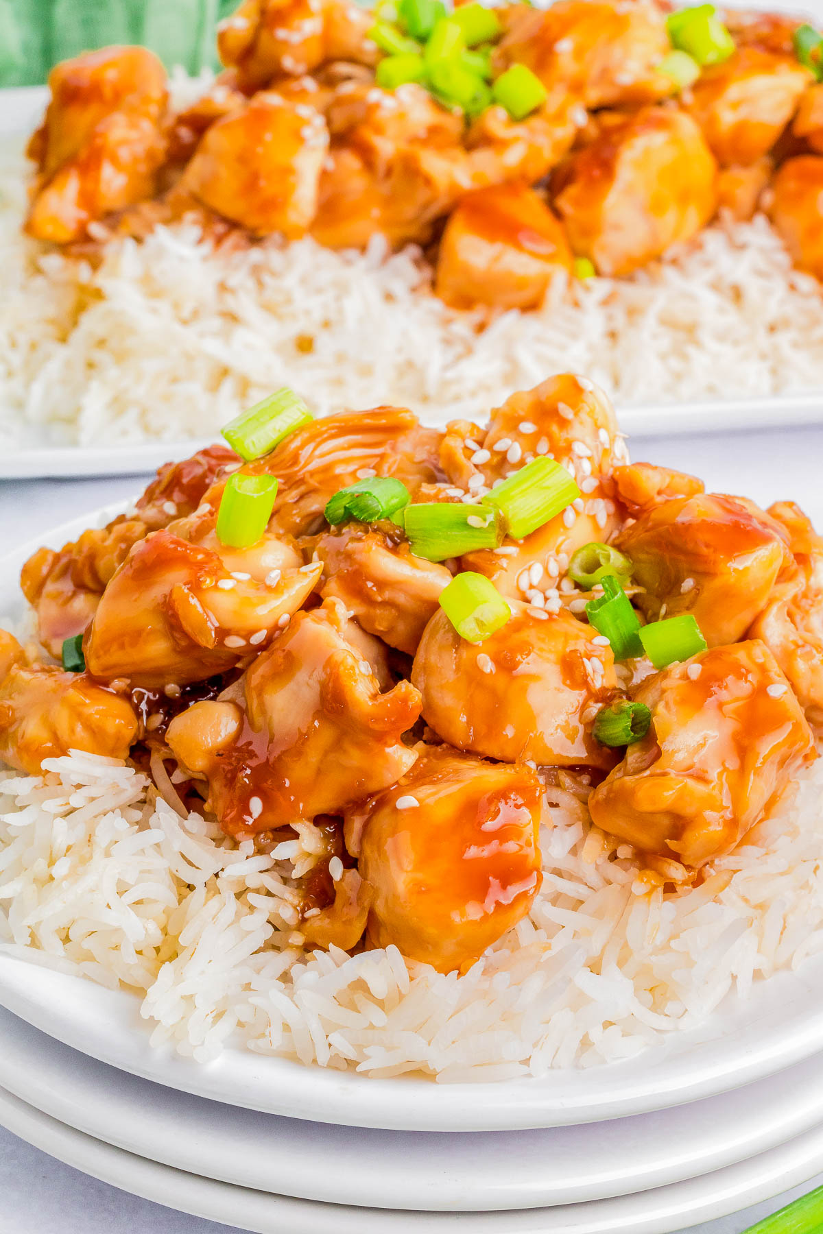 A plate of white rice topped with pieces of orange-glazed chicken, green onions, and sesame seeds.
